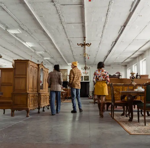 Shoppers browsing wooden furniture in a large secondhand store