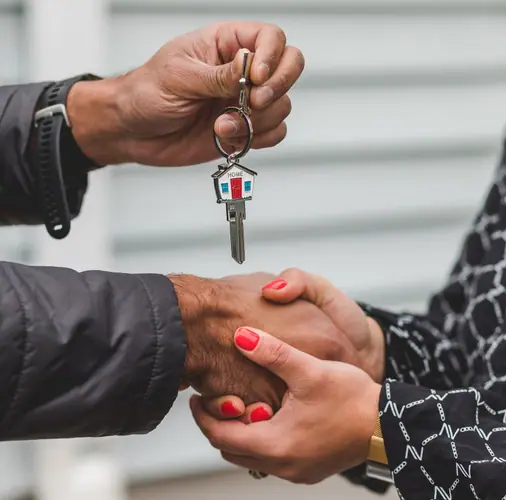 A close-up of a house key being handed over during a handshake